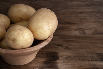 Fototapeta na wymiar Top view of potatoes in wooden bowl on dark wooden background with copy space