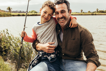 Portrait of father and son sitting beside a lake