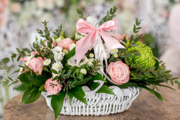Beautiful bouquet of roses in white basket is on a table in flower boutique.