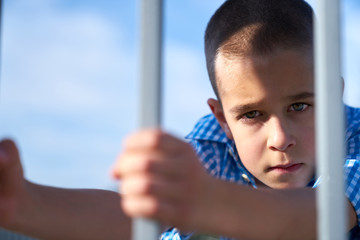 Portrait of a boy looking seriously through a fence 