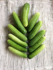 Cucumbers, fresh green leaves arranged in a pattern similar resting on a white cloth.