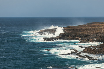 Ocean surf. Big waves crash against stones. Volcanic rock.