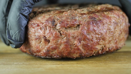 Close-up of a grilled cutlet laid out by the chef in black gloves on a wooden board and then takes it