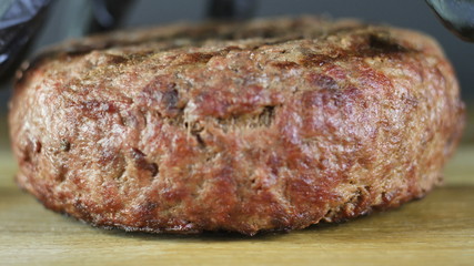 Grilled cutlet lies on a wooden board, the chef in black gloves picks up the cutlet to form a burger