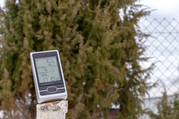 home weather station on the street close-up, shows air temperature, humidity and weather forecast and time on the background of trees