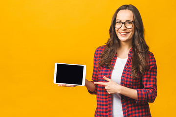 Smiling model with tablet in studio. Showing at tablet. Isolated against yellow background.