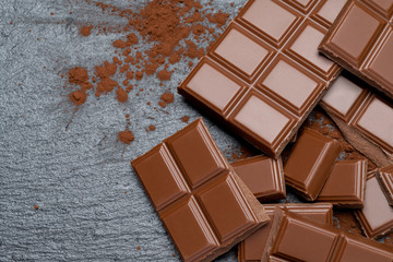 Dark or milk organic chocolate pieces and cocoa powder on dark concrete backgound