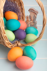 Fototapeta na wymiar Mix of dyed bright Easter eggs in a basket with colorful blue sisal and wooden bunnies on blue surface., selective focus..