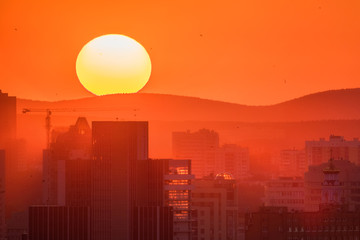 Ekaterinburg, Russia - Jule, 2018: Telephoto lens panoramic shot of cityscape view megalopolis during sunset with giant sun at summer evening