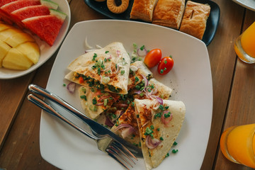 Breakfast table with omelet sandwich, fresh fruit, cookies and orange juice. top view