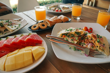 Breakfast table with omelet sandwich, fresh fruit, cookies and orange juice. topview