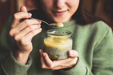 An attractive girl, a brunette, holds a jar with a sweet dessert of kiwi, chia and pineapple in her...