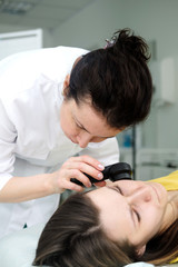 Fototapeta premium Female dermatologist using a professional dermatoscope while doing skin examination, Checking benign moles on face. Dermatologist examining birthmarks and moles on a female patient. Dermatology Clinic