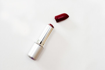 open case with broken Burgundy lipstick on white background