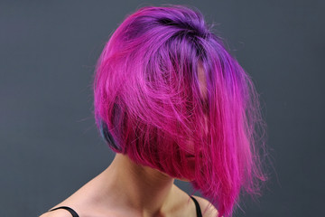 Concept Portrait of a punk girl, young woman with chic purple hair color in studio close up on a colorful background with fluttering hair.