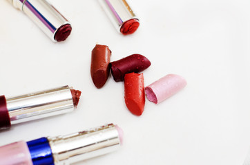 pieces of broken lipstick and open cases lie side by side on a white background