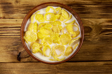 Cornflakes with milk in a bowl on wooden table. Top view