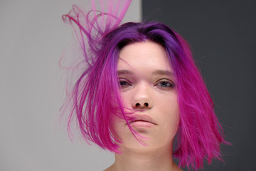 Naklejka premium Concept Portrait of a punk girl, young woman with chic purple hair color in studio close up on a colorful background with fluttering hair.