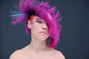 Concept Portrait of a punk girl, young woman with chic purple hair color in studio close up on a colorful background with fluttering hair.