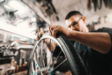 Fototapeta na wymiar Caucasian dedicated man putting tyre on bicycle wheel while standing in workshop.