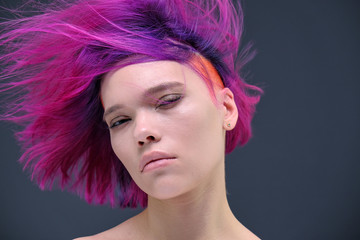 Concept Portrait of a punk girl, young woman with chic purple hair color in studio close up on a colorful background with fluttering hair.