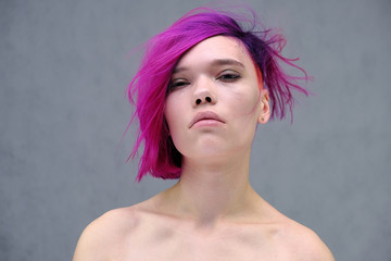 Naklejka premium Concept Portrait of a punk girl, young woman with chic purple hair color in studio close up on a colorful background with fluttering hair.