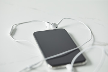 selective focus of earphones connected to smartphone with blank screen on white surface