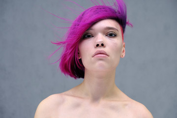 Naklejka premium Concept Portrait of a punk girl, young woman with chic purple hair color in studio close up on a colorful background with fluttering hair.