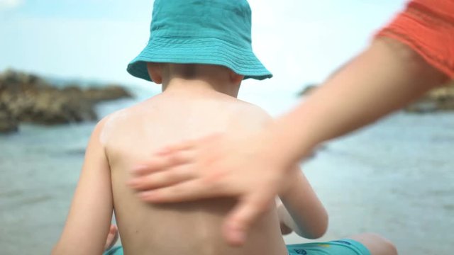 Mother applying sunblock cream on son back at beach.