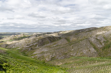 Steep and stony mountains in Kazakhstan, covered with green grass, sand and small stones