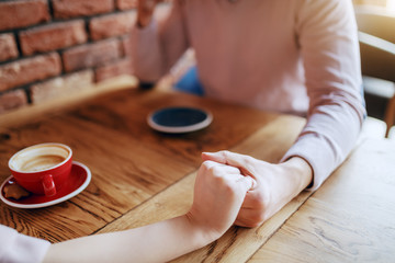 Young couple in love sitting in cafeteria and holding hands. On desk cups with coffee.