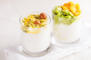 Close-up two glasses with yogurt and fresh fruit puree are standing on white table.
