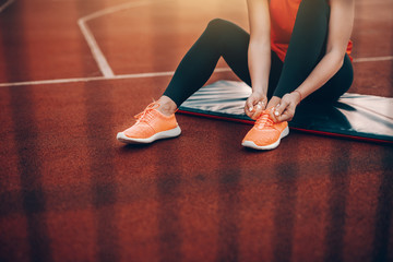Cropped image of Caucasian woman in sportswear sitting on the mat on court and tying shoelace....