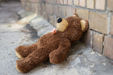 Abandoned teddy bear sitting near a brick wall on the street.
