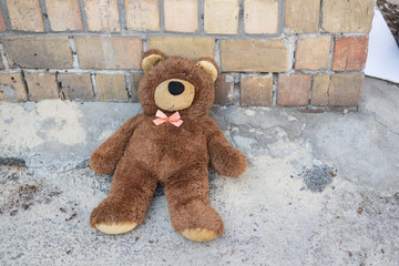 Abandoned teddy bear sitting near a brick wall on the street.