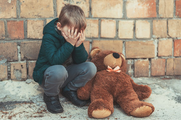 A little boy is crying over a teddy bear outside.