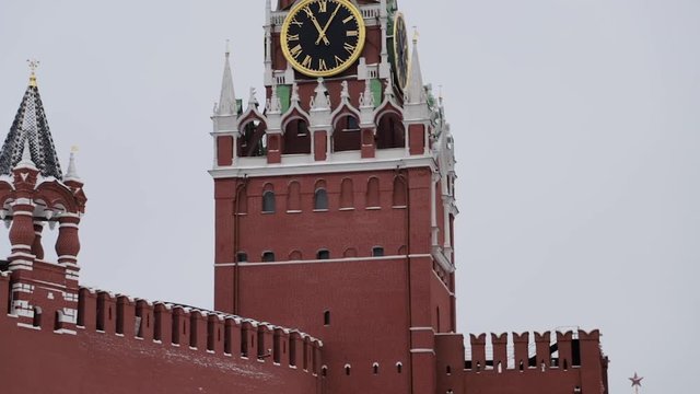 MOSCOW, RUSSIA - DECEMBER, 2018: Gimbal slow motion tilt up shot of Spasskaya clock tower and Moscow Kremlin red brick wall on cloudy winter sky background with russian flag waving