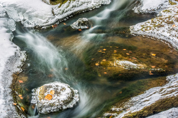 Long exposure shot of the flowing autumn river among the iced stones