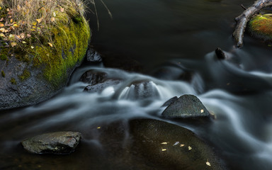 Long exposure shot of the dark flowing river among the stones with green moss