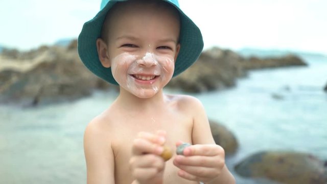 cute boy with sunblock cream in a straw hat on the beach