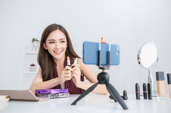 Portrait of asian woman review giveaway product to fan following channel, recording video make up cosmetic at home. Online influencer girl social media marketing live steaming smartphone concept
