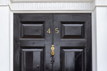 House number 45 with the forty five in bronze on a black wooden door with white door frame