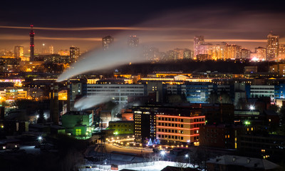 Fototapeta na wymiar Telephoto lens long exposure shot of night cityscape with pipe and chimney emitting steam or smoke