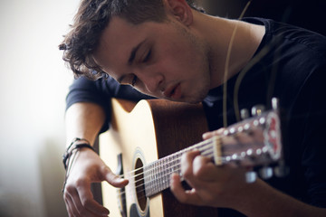 Curly young musician in black clothes performs solo on acoustic six-string guitar