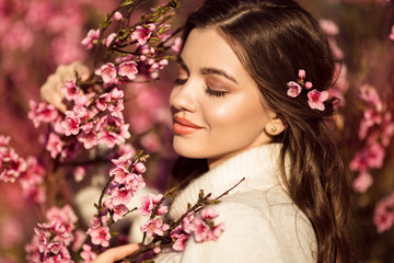 Fototapeta premium Portrait of young beautiful smiling girl posing near blossom tree with pink flowers.