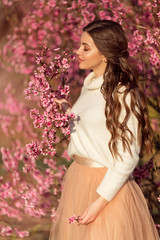 Obraz na płótnie Canvas Portrait of young beautiful girl posing near blossom tree with pink flowers.