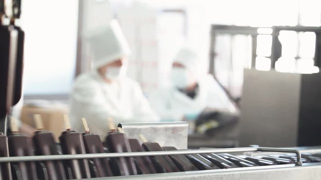 ice cream production, chocolate ice cream is transported on a conveyor, dairy products, workers on blurred background.