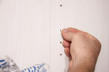 Repair and installation of furniture in the room. Male worker's hands with plugs for drilled holes for shelves on furniture. Details and knots of white furniture.