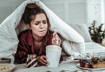 Stressed woman covered with a blanket eating sweets