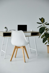 white chair, table with laptop, books, ficus in flowerpot on grey